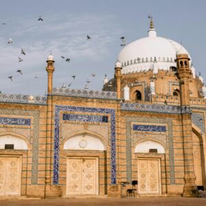 A stunning view of the Bahauddin Zakariya Shrine in Multan with flying pigeons against a clear sky.